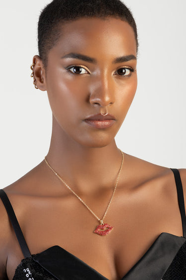 woman wearing a gold chain necklace with a red lips pendant against a black outfit