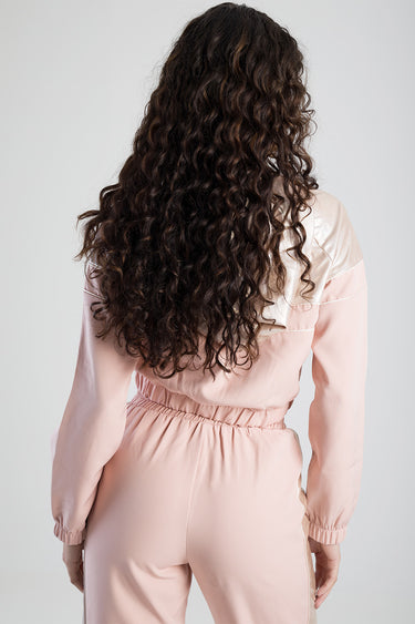woman with long dark curly hair wearing a light pink tracksuit top with elastic waist and cuffs, back view