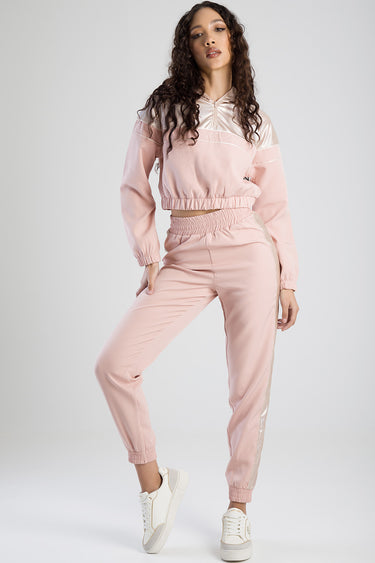woman wearing a pink satin cropped track top with long sleeves and elastic hem, paired with matching jogger pants and white