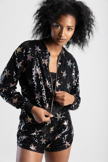 woman wearing a black sequin bomber jacket with multicolored stars and a front zipper