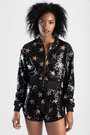 woman wearing a black sequin bomber jacket with multicolor stars, gold zip front and elastic waistband