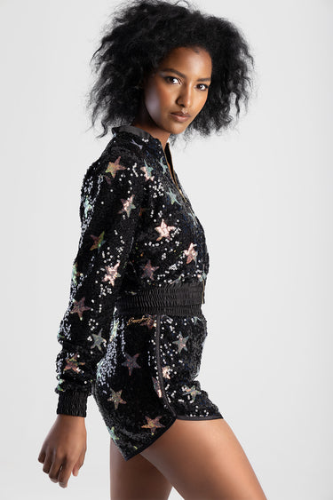 model wearing a black sequin bomber jacket with multicolour stars, zip front, ribbed cuffs and hem, in a side pose