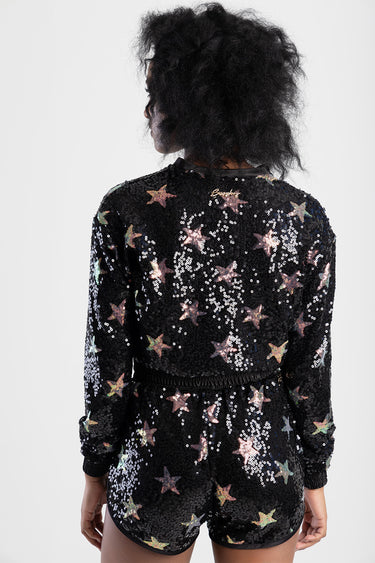 back view of a woman wearing a black sequin bomber jacket with multicolor star patterns