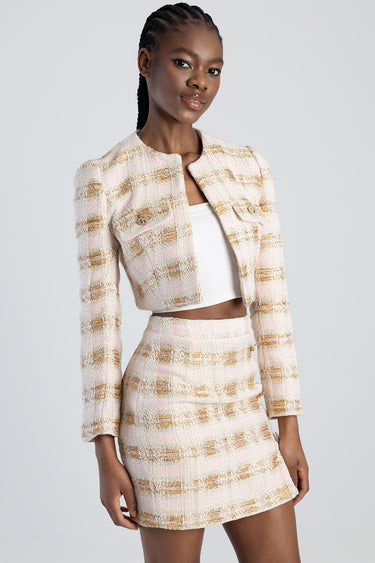 woman wearing a pink and cream tweed cropped jacket with gold stripes and matching mini skirt over a white top