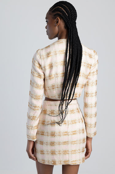 woman shown from behind in a pink and beige tweed cropped jacket and matching skirt, with long braids