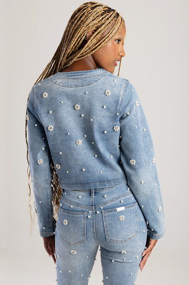back view of a woman in a light blue denim jacket with pearl embellishments, paired with matching jeans
