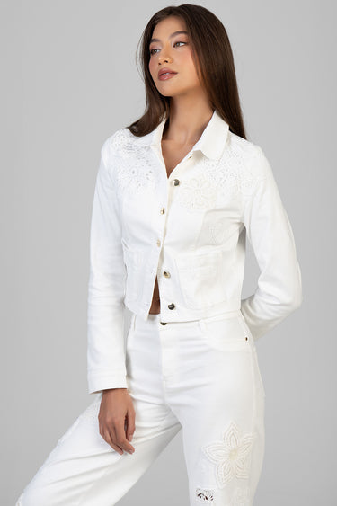 woman wearing a white denim jacket with lace floral appliques on shoulders and pockets, paired with white jeans.