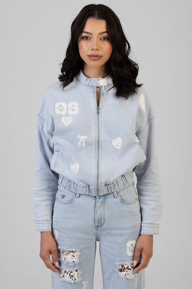 woman wearing light blue denim bomber jacket with white lace patches, zip front, elastic hem, paired with matching jeans