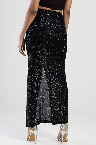Blue Jean Traders sequin maxi skirt shown from back with a side slit and metallic sparkle, paired with nude heels.