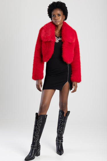 woman wearing a bright red faux fur jacket over a black mini skirt with a front slit, paired with tall black studded boots