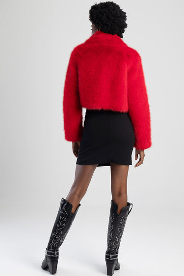 woman wearing a bright red fluffy cropped jacket over a black mini skirt and studded knee high boots back view