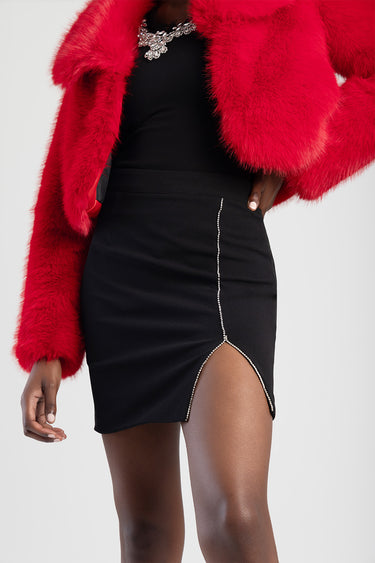 woman wearing black mini skirt with rhinestone trim and a small side slit, paired with red faux fur jacket