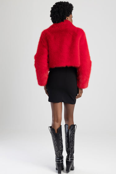 woman in a bright red fuzzy cropped jacket paired with a black mini skirt and studded knee high boots, back view