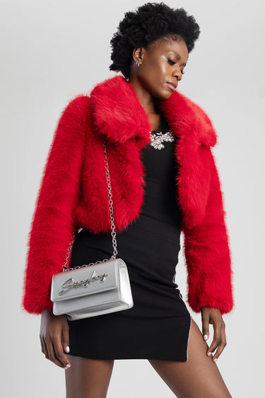 woman wearing a bright red faux fur jacket over a black mini dress, carrying a silver chain bag