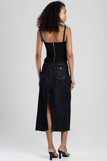 woman in a black sleeveless top and dark denim midi skirt with a back slit and visible zipper at the waist.