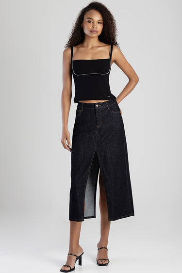 woman models a dark denim midi skirt with a front slit and contrast stitching, paired with a black sleeveless top.