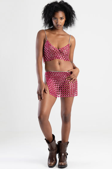 model wearing a pink jeweled mesh bralette and matching mini skirt with brown boots