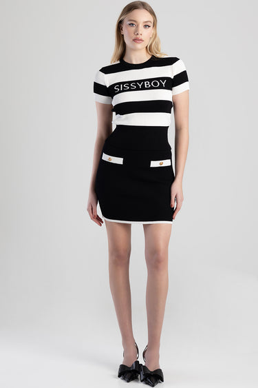 model wearing a black and white striped knit top and a black mini skirt with white trim and gold button pocket details