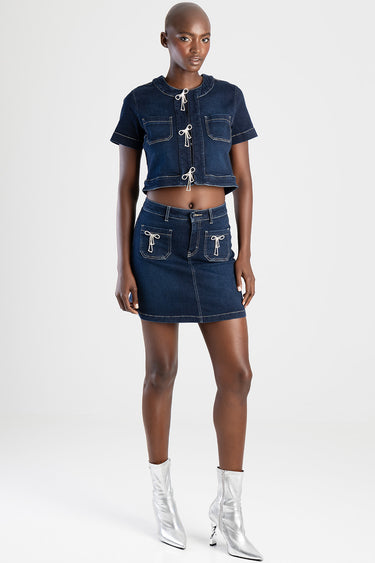 woman wearing a dark blue denim cropped top with lace ties and matching mini skirt with front pockets and white stitching