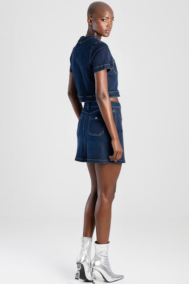 woman wearing a dark blue denim mini skirt seen from the side, with a matching cropped denim top and silver ankle boots