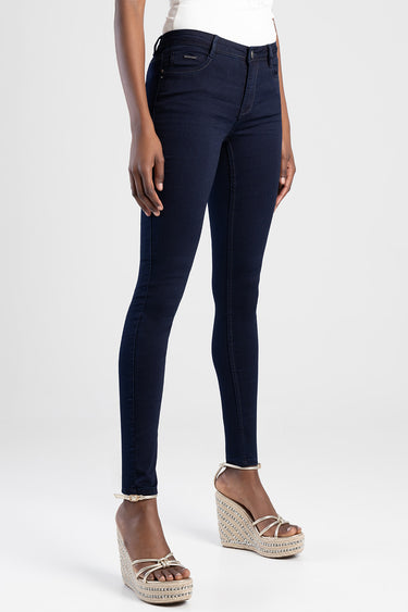 woman wearing dark blue skinny jeans and beige wedge sandals against a light backdrop