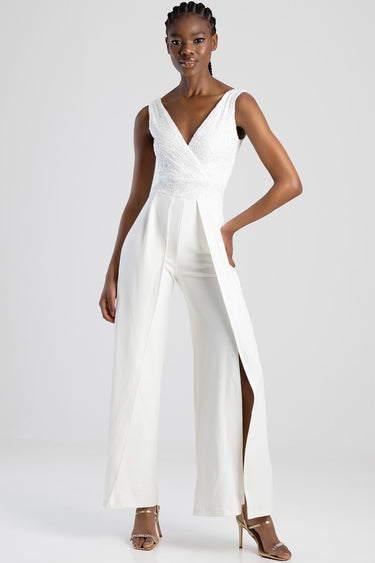 white lace bodice jumpsuit by blue jean traders, deep v neck, wide leg pants with front slit, paired with gold heeled sandals