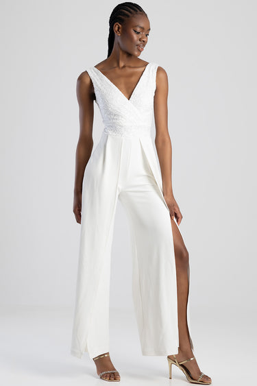 woman in a white lace bodice jumpsuit with sleeveless v neck, wide leg pants with a front slit, gold strappy sandals