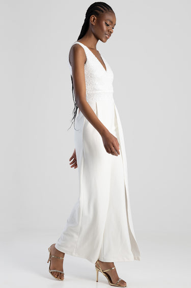 side view of a woman in a white lace bodice jumpsuit with wide legs and gold strappy heels