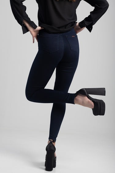 back view of a model in dark indigo skinny jeans and a black top with black platform heels