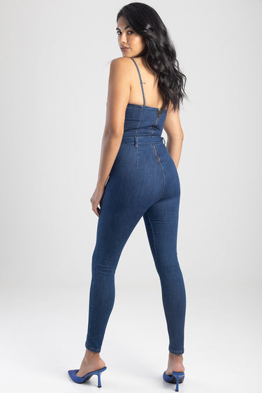 woman wearing a blue denim jumpsuit with slim straps and cinched waist, back view, paired with blue heeled sandals