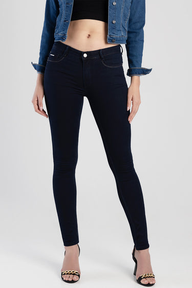 woman in dark navy skinny jeans with a cropped denim jacket and black crop top, standing in sandals