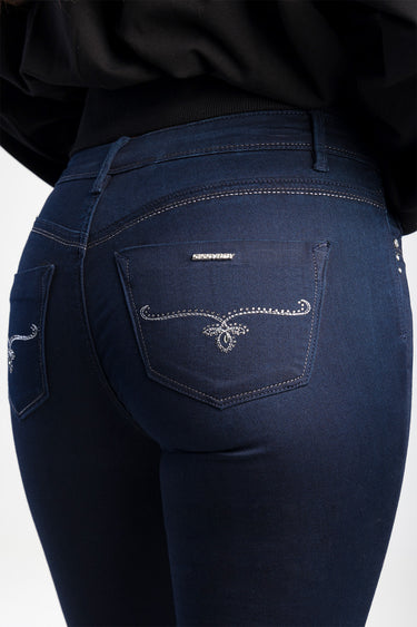 back view of dark blue skinny jeans with white embroidered scroll design on pockets and a small metal brand badge