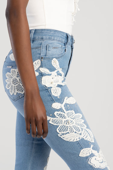woman wearing light blue jeans with white floral crochet patches along the leg and a small blue jean traders logo on the