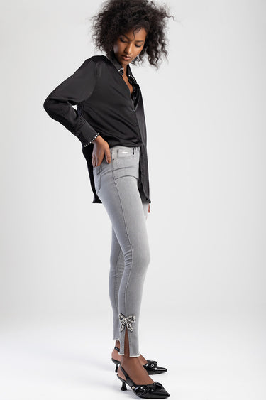 woman wearing a black long sleeve buttoned shirt and light grey straight jeans with a bow at the ankle