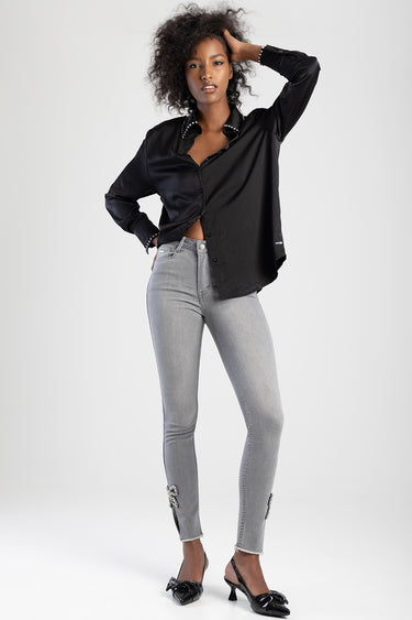 woman wearing light grey denim jeans with bow embellishments at the ankles, paired with a black buttoned shirt and heels