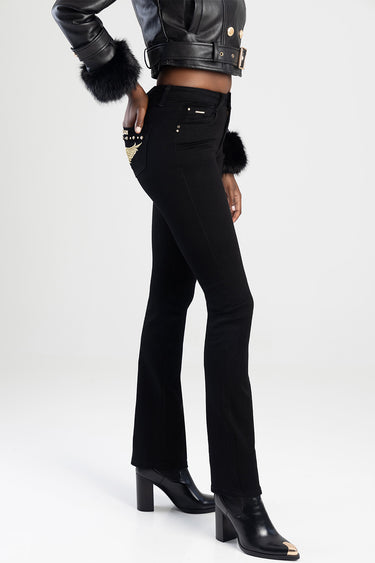 side view of a model wearing black bootcut jeans with gold wing embroidery on the back pocket and metal studs, paired with