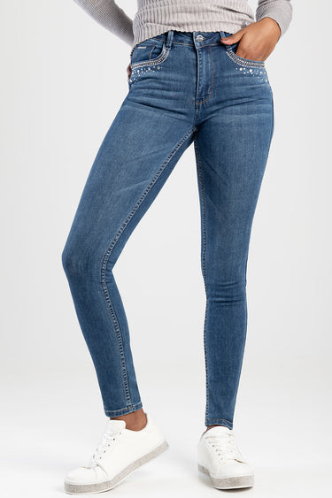 woman wearing blue skinny jeans with rhinestone trim at pockets, paired with a light grey sweater and white sneakers