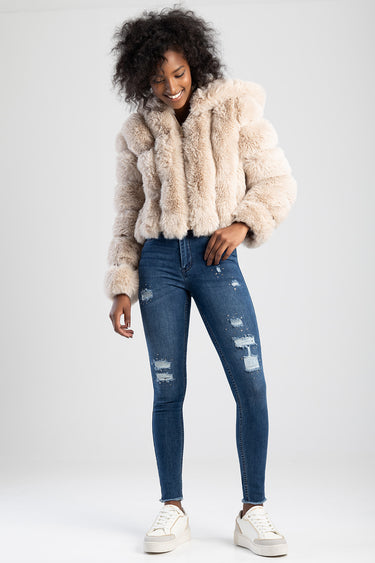 woman in a beige faux fur jacket and distressed blue jeans with white sneakers