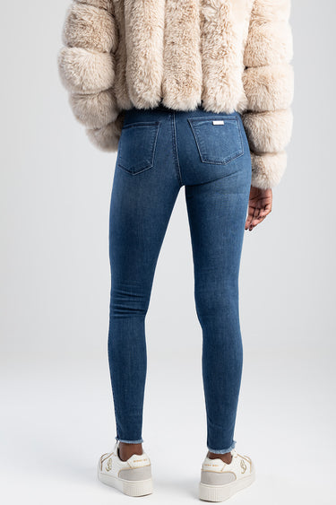 back view of person in blue denim jeans with back pockets and a beige fluffy coat and white sneakers