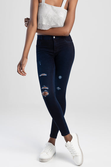 woman in dark wash distressed jeggings with ripped knees, paired with white sneakers and a silver crop top