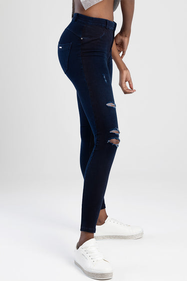 model wearing dark indigo blue jean traders jeggings with distressed knees, side pockets, and white sneakers, side view