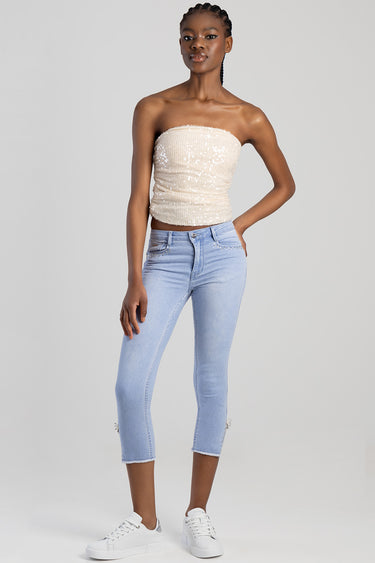 woman in light blue capri jeans with rhinestone pockets, paired with a beige sequined strapless top and white sneakers
