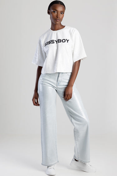 female model wearing a white sequin short sleeve top with a black logo and light blue wide leg jeans with white sneakers
