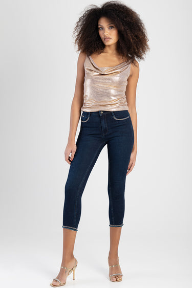 woman modelling dark blue capri jeans with stitching and silver trim, paired with a metallic draped sleeveless top