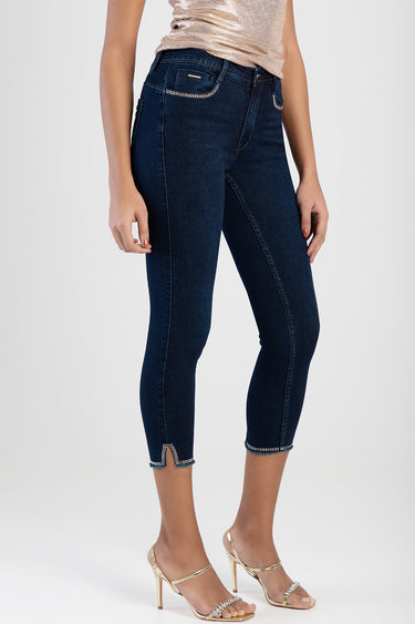 woman wearing dark blue denim capri jeans with rhinestone trim on pockets and cuffs, cropped length, paired with gold heels