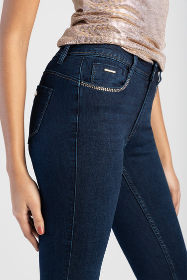 side view of woman in dark blue denim jeans with rhinestone trim along back pocket and a small brand tag.
