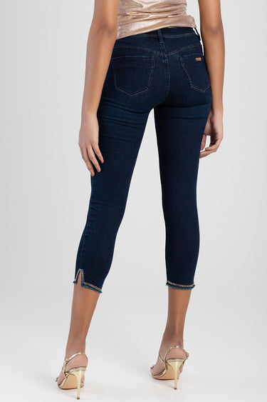 woman wearing dark blue capri jeans with back pockets and beaded hems at the ankles, paired with gold heels