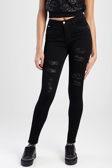 woman wearing black distressed skinny jeans with sequin patches and a silver button, paired with black sneakers