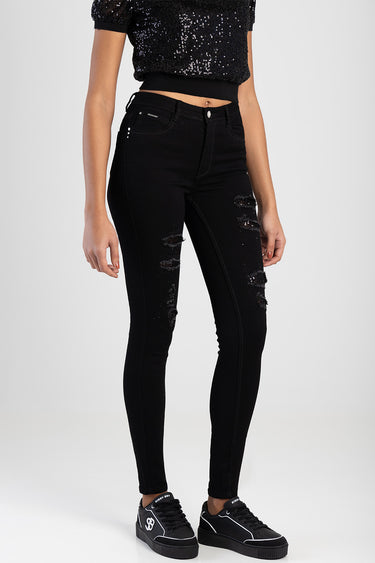 woman wearing black skinny jeans with ripped knees and silver hardware, paired with a black sequined top and black sneakers