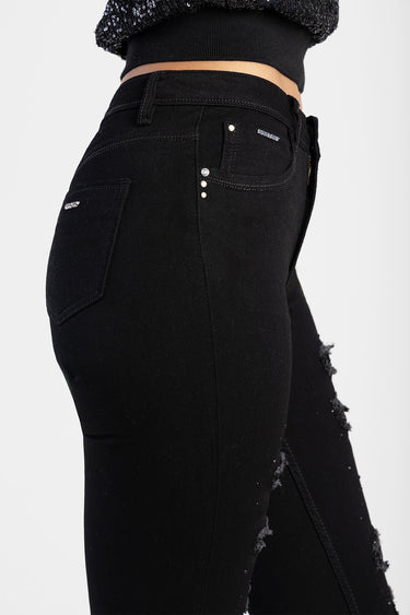 side view of black denim jeans with distressed knees, silver rivets and small brand tags on pockets